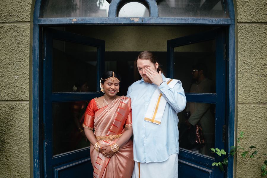 A couple in a blue doorway, the groom laughing